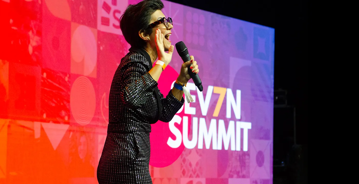 Palestrante no palco do Seven Summit com o painel colorido da identidade ao fundo